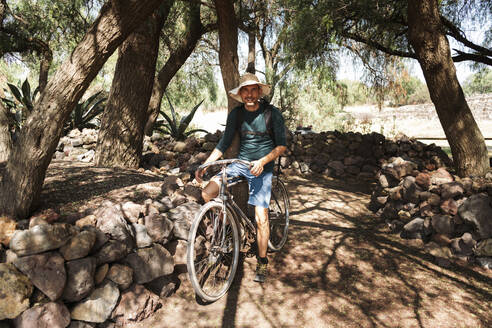 Mature man wearing hat riding bicycle on dirt road in Teotihuacan, Mexico - JMPF00270