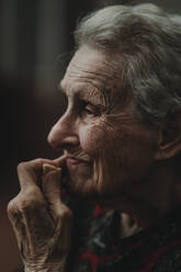 Seitenansicht einer nachdenklichen älteren Frau mit grauem Haar, die ihr faltiges Gesicht berührt und beim Essen eines Kekses an die Vergangenheit denkt - ADSF08236