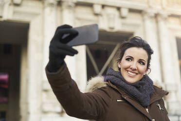 Junge fröhliche Frau in Winterkleidung nimmt ein Selfie mit Smartphone im Freien in Mailand Italien - ADSF08244