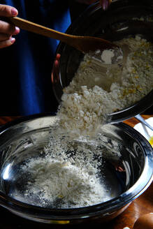 Unbekannte Frau verschüttet Weizenmehl in eine Metallschüssel bei der Zubereitung von Gebäck zu Hause - ADSF08349