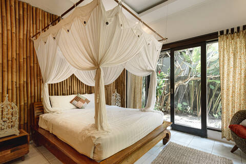 Bright interior of bedroom in hotel with bamboo wall and cozy canopy bed in Bali stock photo