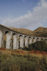 Niedriger Winkel des alten Eisenbahnviadukts im schottischen Hochland gegen Berge und blauen bewölkten Himmel an einem Herbsttag - ADSF08357