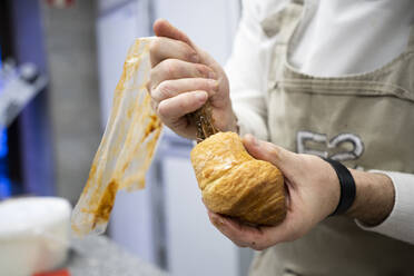 Mann in Schürze und weißer Uniform, der drinnen ein frisches Croissant mit Schokoladencreme füllt - ADSF08370