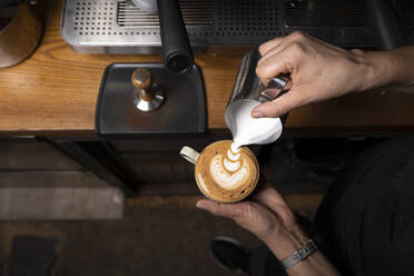 Von oben Ernte Hände der professionellen Mitarbeiter bereitet Cappuccino mit Muster auf der Oberseite in Coffee-Shop - ADSF08379