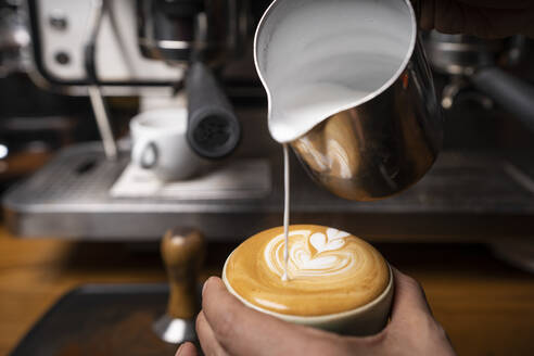 Von oben Ernte Hände der professionellen Mitarbeiter bereitet Cappuccino mit Muster auf der Oberseite in Coffee-Shop - ADSF08381
