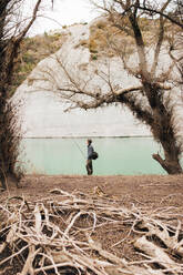 Seitenansicht eines Mannes mit Rucksack, der am Seeufer steht und an einem sonnigen Tag in der Natur angelt - ADSF08409