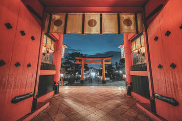 Low angle of religious shrine with torii gates and red wooden walls in Kyoto in evening - ADSF08437