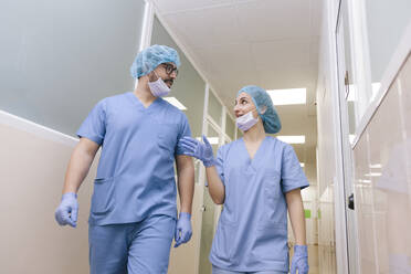 Fellow surgeons man and woman chat while walking towards the operating theater - ADSF08499