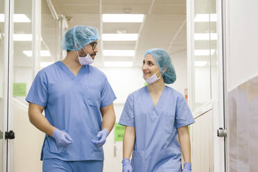 Fellow surgeons man and woman chat while walking towards the operating theater - ADSF08500