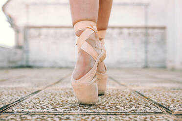 Crop female dancer wearing pointe shoes standing on tiptoes on weathered stone ground and demonstrating dancing position - ADSF08531