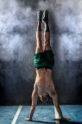 Full length muscular man doing handstand against white dust cloud during functional workout in gym - ADSF08534