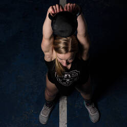 Von oben starke junge Frau mit schwerer Kettlebell beim intensiven Training im Fitnessstudio - ADSF08540