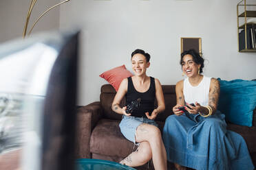 Cheerful lesbian couple watching TV on sofa - MEUF01749