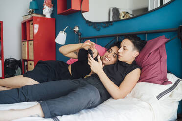 Lesbisches Paar telefoniert auf dem Bett liegend - MEUF01751