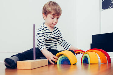 Lustiges Kind spielt mit Spielzeug und sitzt auf dem Boden im Zimmer - ADSF08626