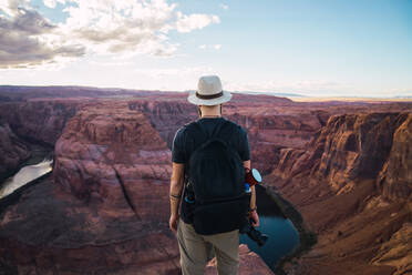 Rückansicht eines bärtigen Mannes mit Rucksack, der eine Fotokamera hält, um Bilder von einem schönen Canyon und einem ruhigen Fluss an einem sonnigen Tag an der Westküste der USA zu machen - ADSF08631