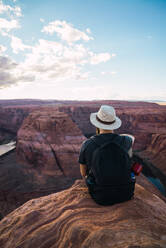 Back view of bearded guy with backpack looking at beautiful canyon and calm river on sunny day on West Coast of USA - ADSF08632