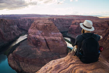 Back view of bearded guy with backpack looking at beautiful canyon and calm river on sunny day on West Coast of USA - ADSF08633