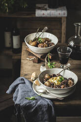 Traditionelles Gericht Boeuf Bourgingnon, serviert mit Nudeln in Schüsseln auf einem Holztisch - ADSF08649