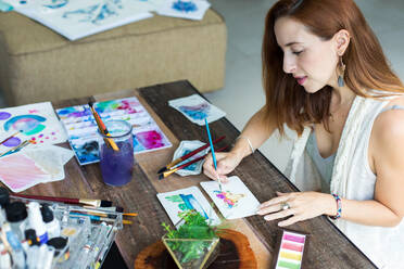 Latin artist painting with watercolor in her studio - ADSF08692