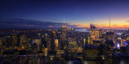 Wide angle drone view of illuminated skyscrapers located in downtown of modern city against cloudy sundown sky - ADSF08722