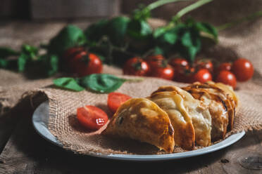 From above of traditional Spanish homemade turnovers served in bowl on rustic wooden table with fresh spinach and tomatoes - ADSF08724