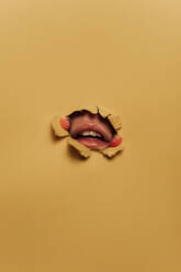 Gesichtsloses Modell, das seine Lippen demonstriert, während es mit den Händen ein Loch in gelbes Papier reißt - ADSF08736