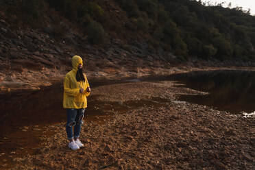 Junge Frau in gelbem Regenmantel beim Spaziergang in der Natur - ADSF08754
