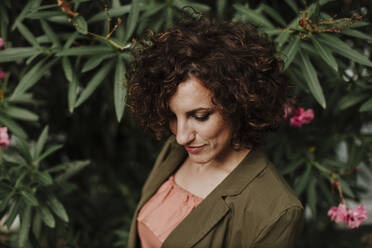 Close-up of mid adult woman with curly hair against plants in park - GMLF00397