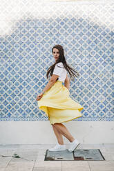Beautiful woman with long hair spinning on street against tiled wall in city - DCRF00569