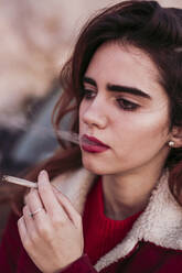 Nahaufnahme einer nachdenklichen schönen Frau beim Rauchen einer Zigarette - LJF01714