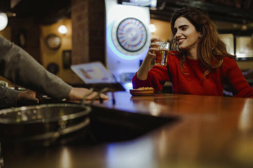 Lächelnde schöne Frau hält Bierglas im Gespräch mit Barkeeper im Restaurant - LJF01723