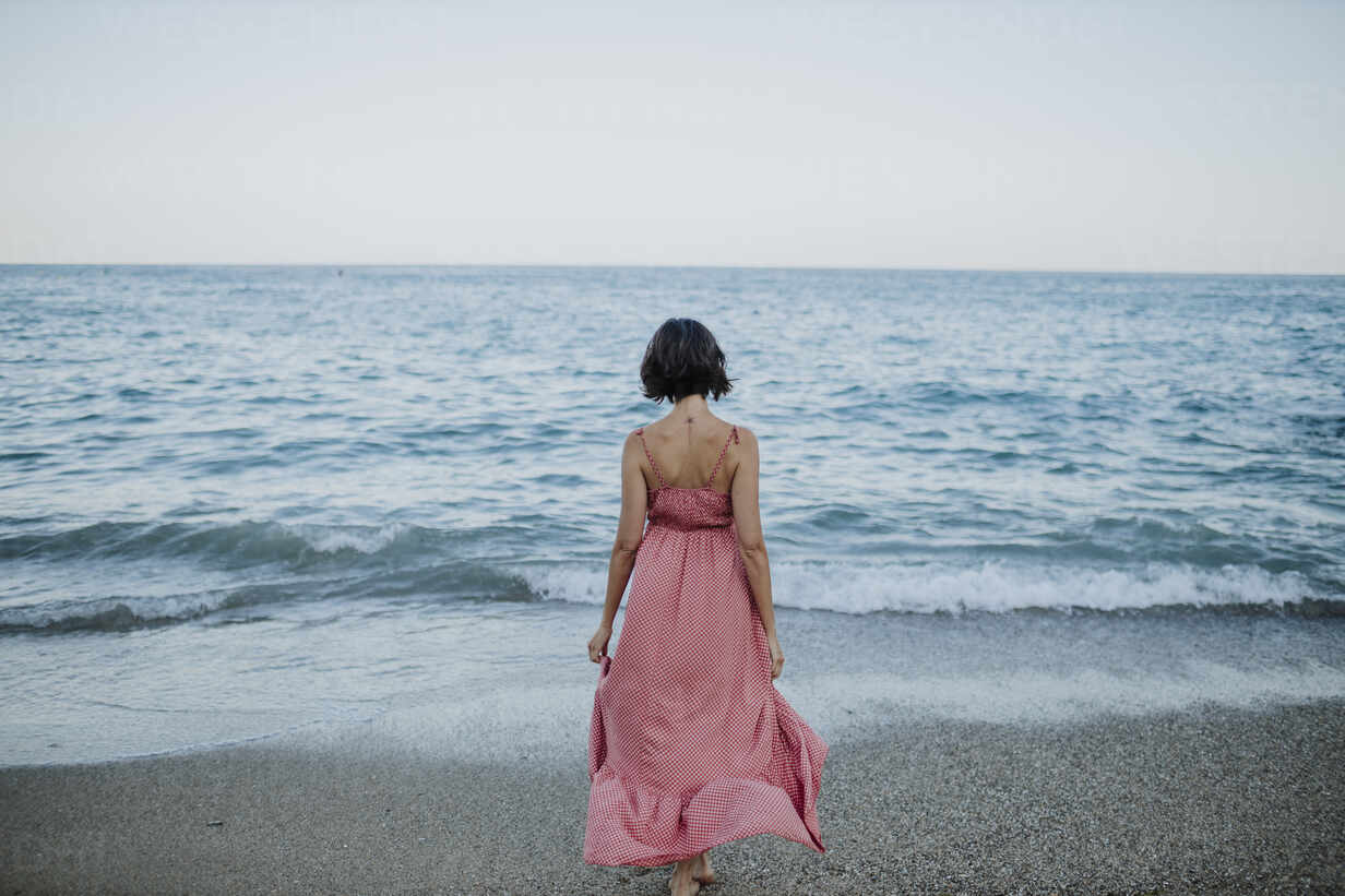 Woman wearing dress walking towards sea at beach against clear sky ...