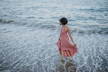 Mid adult woman wearing dress standing in sea during sunset - GMLF00406