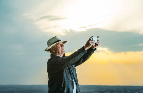 Älterer Mann fotografiert bei Sonnenuntergang mit seinem Smartphone - OCMF01596