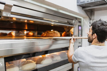 Bäcker backt Brot im Ofen in einer Bäckerei - MRRF00176