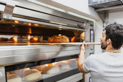 Baker baking bread in oven at bakery - MRRF00176