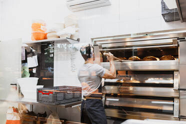 Bäcker backt Brot im Ofen in einer Bäckerei - MRRF00193