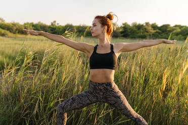 Frau übt Krieger zwei Yoga-Pose auf grasbewachsenen Feld - EGAF00622
