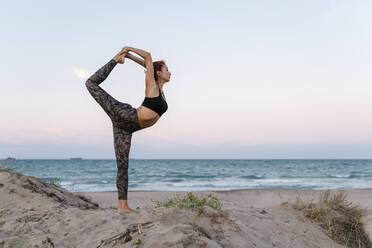 Young woman practicing yoga on beach against clear sky - EGAF00633