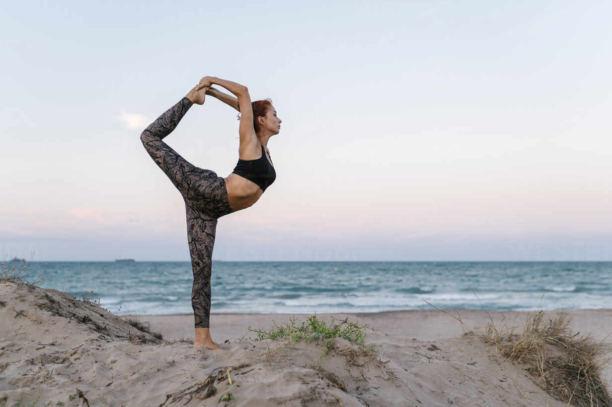 Young woman practicing yoga on beach against clear sky stock photo
