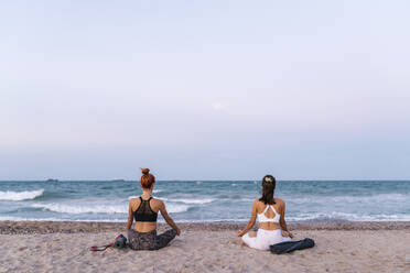 Young women meditating on beach against clear sky during sunset - EGAF00636