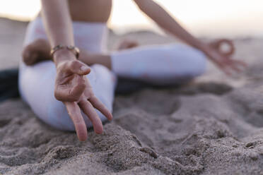 Close-up of young woman meditating on sand at beach - EGAF00637