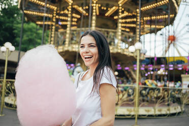 Fröhliche junge Frau mit Zuckerwatte im Vergnügungspark stehend - OYF00181