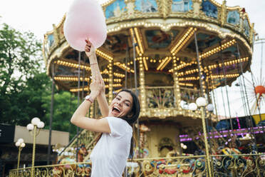 Cheerful beautiful woman holding cotton candy screaming while standing in amusement park - OYF00184
