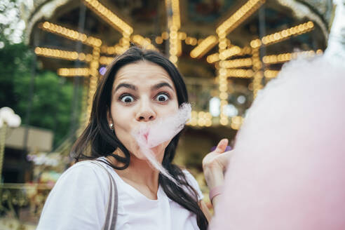 Nahaufnahme einer jungen Frau, die Zuckerwatte an einem Karussell im Vergnügungspark isst - OYF00187