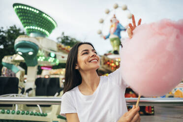 Lächelnde junge Frau mit Zuckerwatte in der Hand im Vergnügungspark - OYF00189