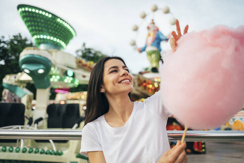 Lächelnde junge Frau mit Zuckerwatte in der Hand im Vergnügungspark - OYF00189