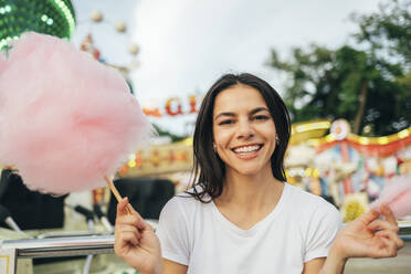 Smiling beautiful woman holding cotton candy in amusement park - OYF00192