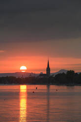 Deutschland, Baden-Württemberg, Radolfzell, Bewölkter Himmel über dem Bodensee bei stimmungsvollem Sonnenuntergang mit Turm des Radolfzeller Münsters im Hintergrund - ELF02167